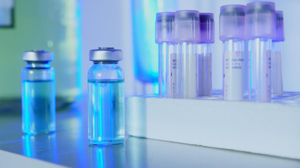 Have Question? Book A Consult Vials and test tubes with blue liquid in a laboratory setting under fluorescent light.